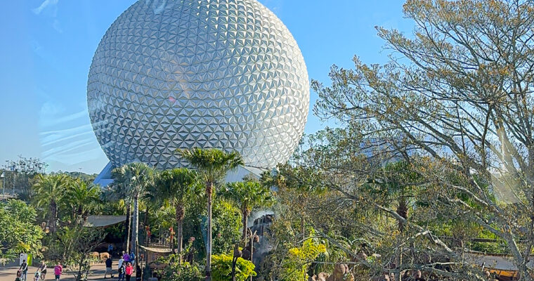 Spaceship Earth at EPCOT with trees in the foreground on bright, sunny day.