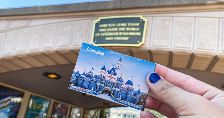 Hand holding a ticket to Disneyland Park with park entrance in the background on sunny day.