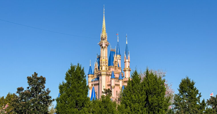 Cinderella Castle at Magic Kingdom in Walt Disney World emerging from trees on a clear, sunny day.